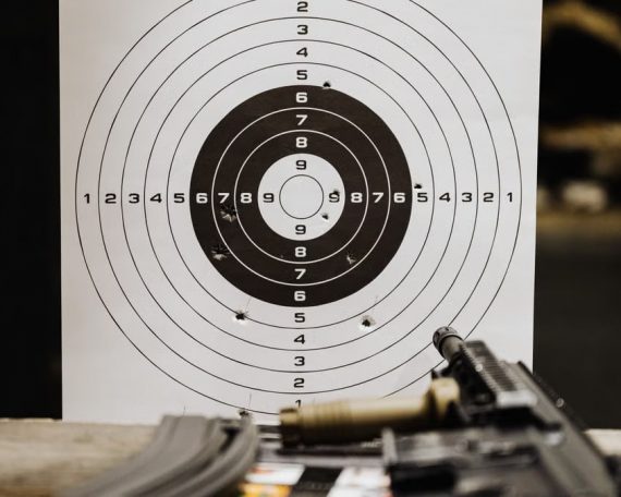 Close-up of a shooting target with bullet holes on a range table next to a rifle.